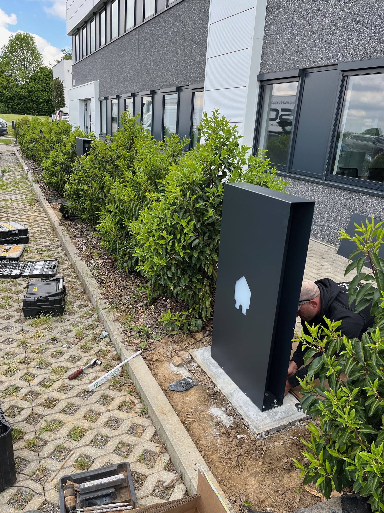Technicien scellant une borne de rechargement au pied d'un bâtiment